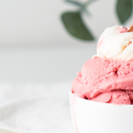 A photograph of a bowl of raspberry sorbet with a golden spoon.
